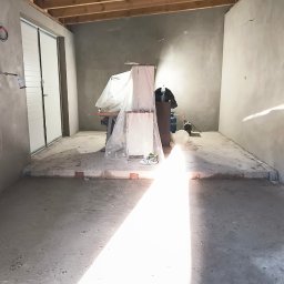 FIRMA BUDOWLANO-HANDLOWO-USŁUGOWA BAZ-BUD Mariusz BAZAN - Wnętrze pomieszczenia w trakcie prac wykończeniowych, widoczne surowe ściany, drewniany strop, zabezpieczone meble folią i sprzęt budowlany.