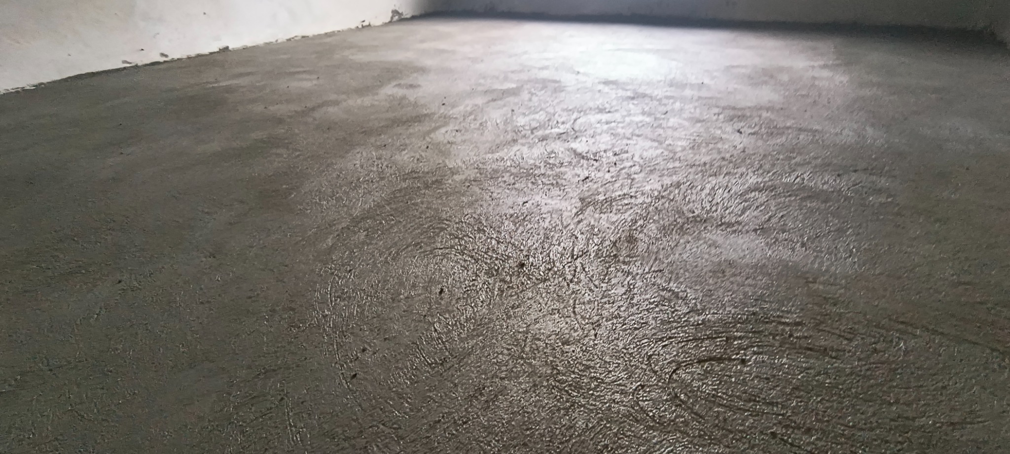 Świeżo wylana, mokra wylewka betonowa na podłodze w pomieszczeniu w trakcie prac wykończeniowych, widoczne ślady po narzędziach.