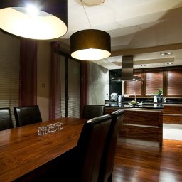 INVOST SPÓŁKA Z OGRANICZONĄ ODPOWIEDZIALNOŚCIĄ - Nowoczesna jadalnia z drewnianym stołem, skórzanymi krzesłami i otwartą kuchnią w tle, oświetlona wiszącymi lampami z abażurami.