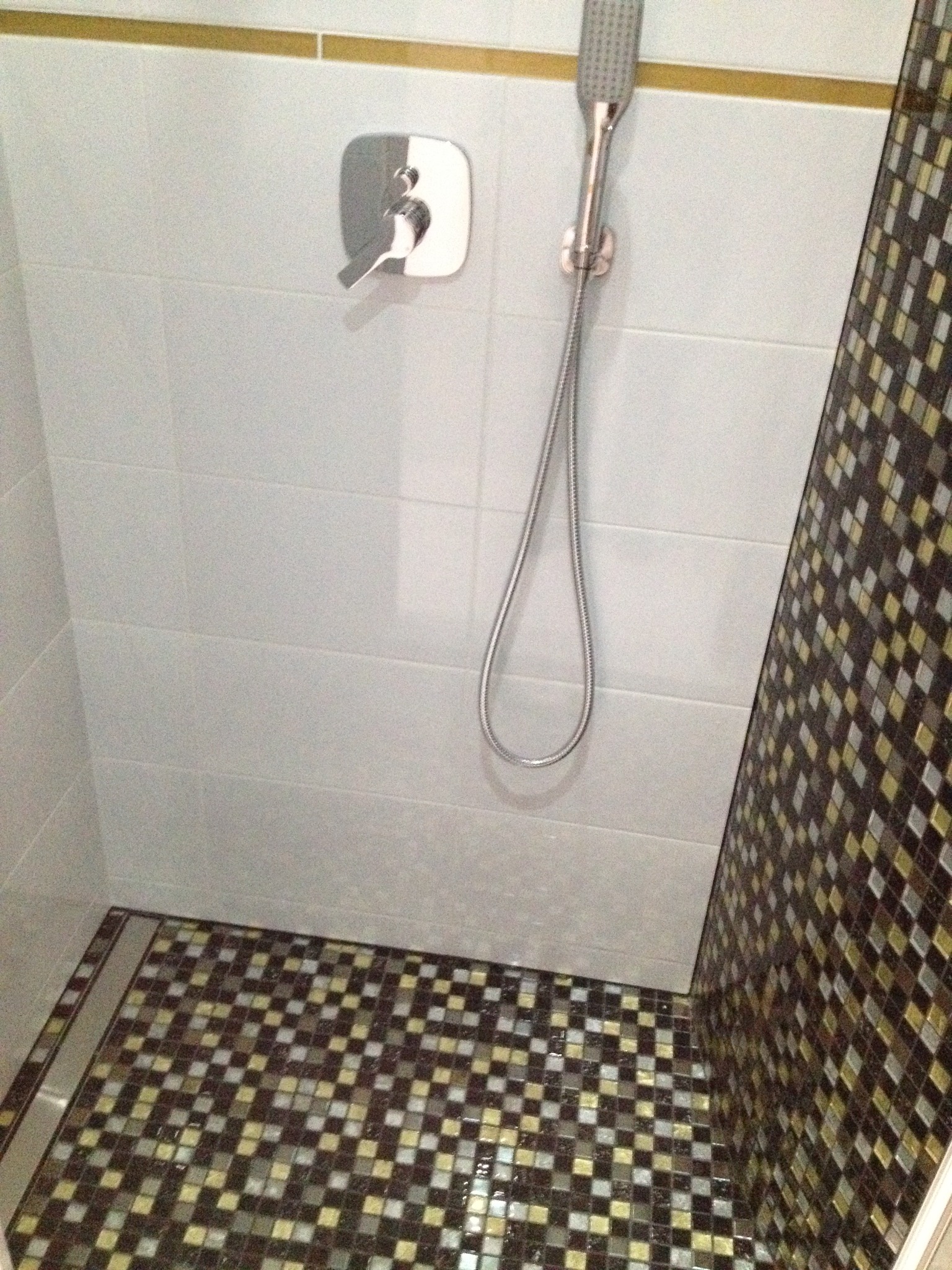 Ukończona kabina prysznicowa z mozaiką na podłodze i jednej ścianie, białe płytki na pozostałych ścianach, chromowana armatura i deszczownica.