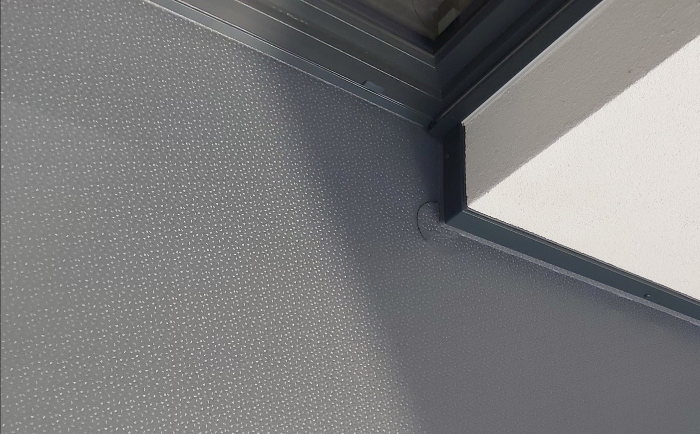Szczegółowe ujęcie narożnika zabudowanego balkonu z szarą, teksturowaną ścianą i białym sufitem, widoczne profile aluminiowe.