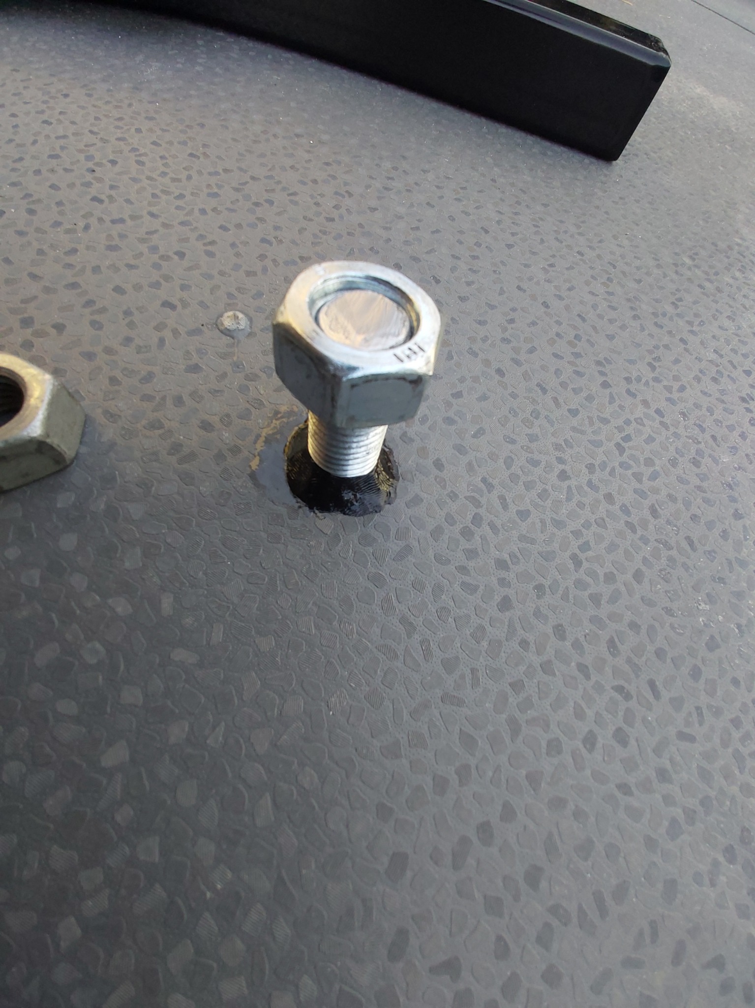 Szczegółowy widok śruby i nakrętki mocującej element konstrukcyjny na szarej, teksturowanej powierzchni, prawdopodobnie podczas montażu.