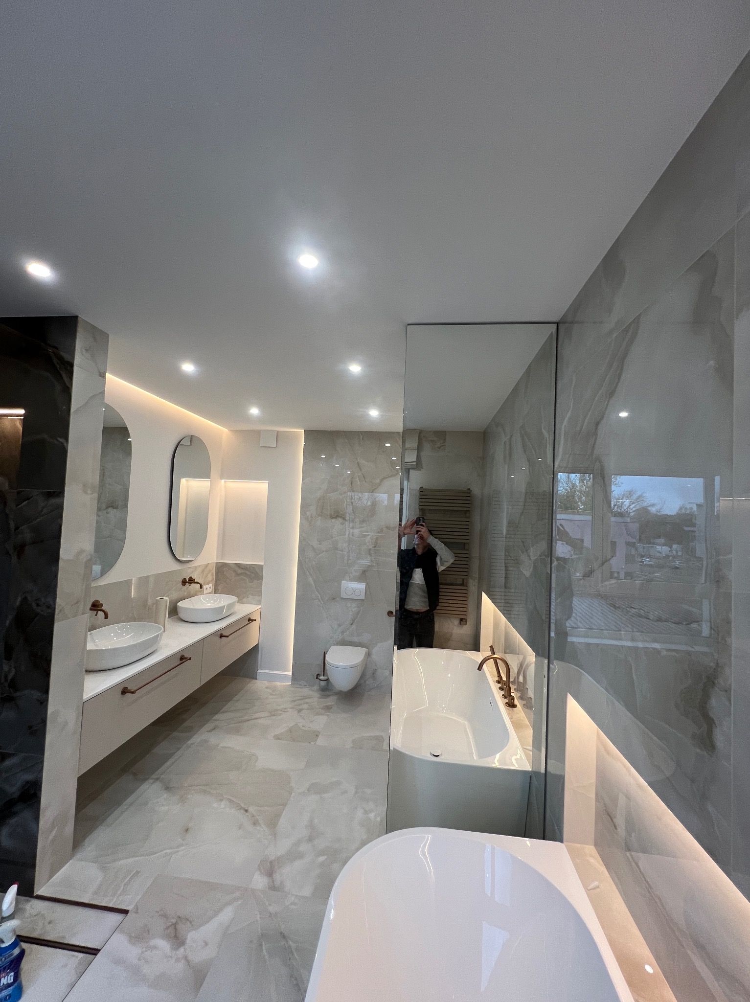 Nowoczesna łazienka z marmurowymi płytkami, podwójną umywalką nablatową, owalnymi lustrami z podświetleniem LED i wolnostojącą wanną w minimalistycznym stylu, widok z perspektywy szerokokątnej.