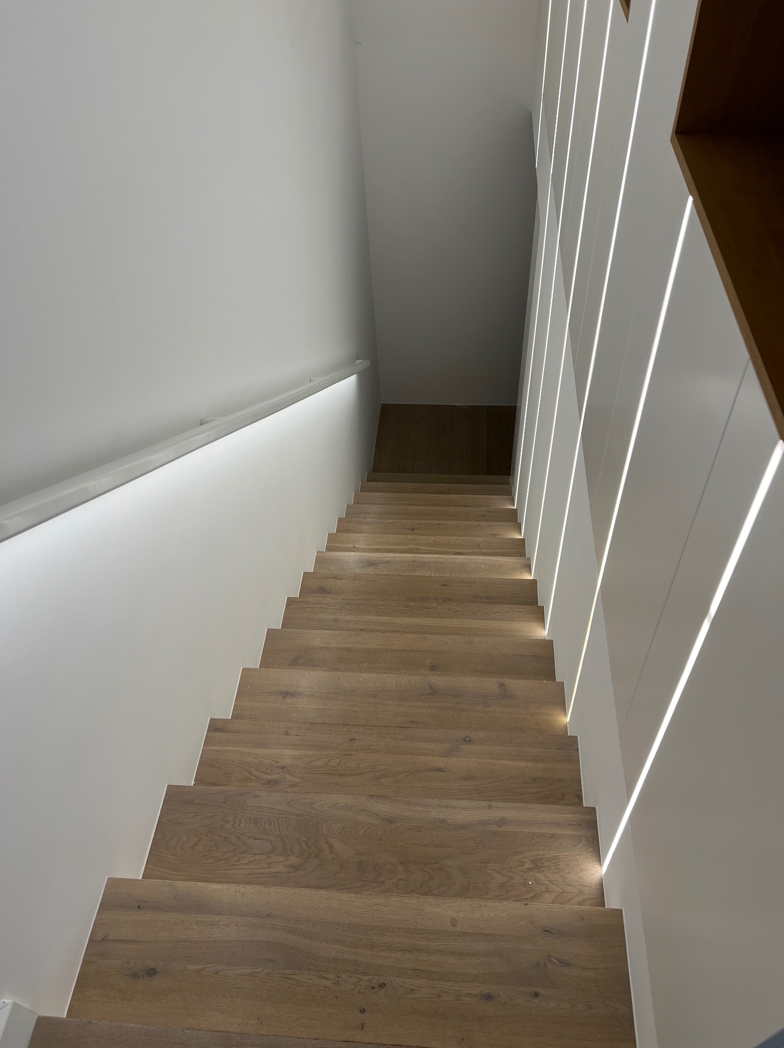 Nowoczesne schody drewniane z oświetleniem LED wzdłuż stopni i na ścianie, widok z góry, minimalistyczny design.