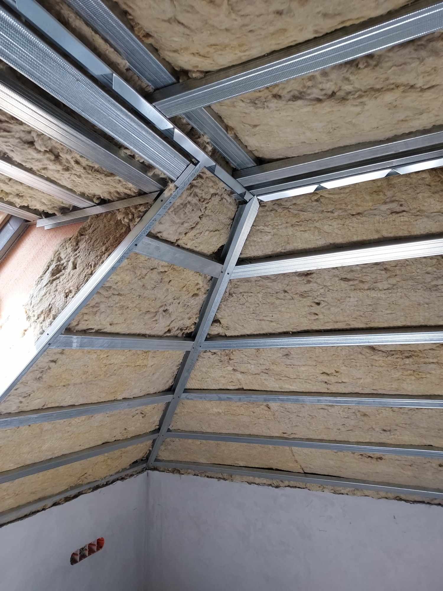 Montaż izolacji z wełny mineralnej w poddaszu w Żywcu, widoczne metalowe profile konstrukcyjne sufitu podwieszanego.