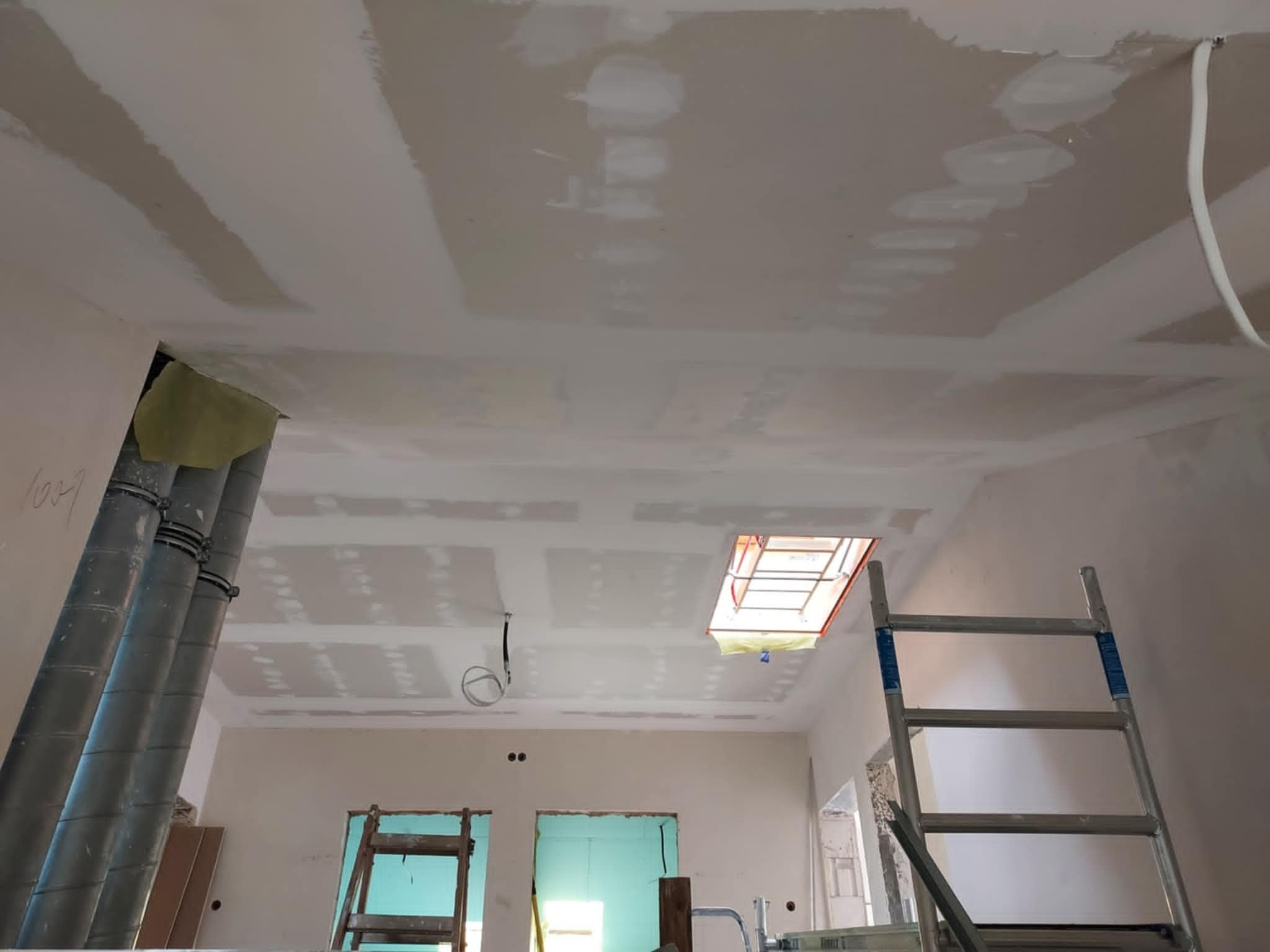 Sufit z płyt gipsowo-kartonowych w trakcie prac wykończeniowych, widoczne łączenia płyt wymagające szpachlowania, fragment instalacji wentylacyjnej i drabina
