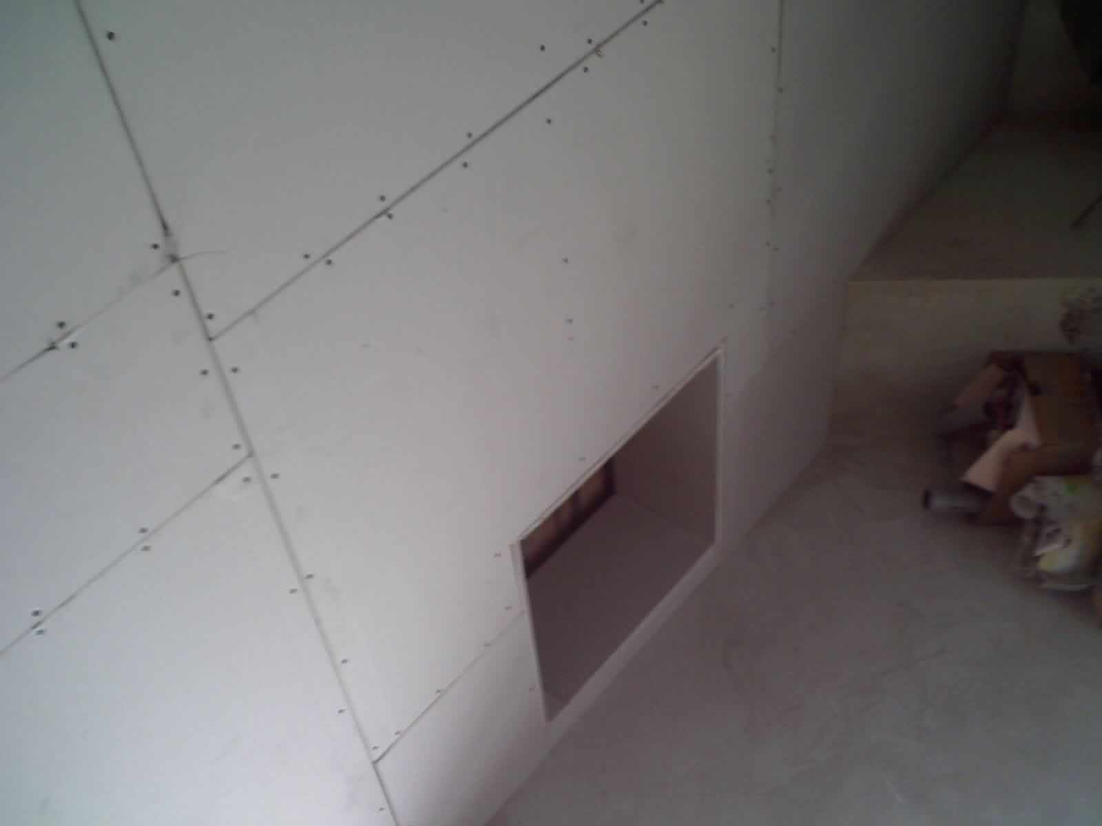 Ściana poddasza wykończona płytami gipsowo-kartonowymi, z widocznym otworem rewizyjnym i śladami szpachlowania na łączeniach płyt.