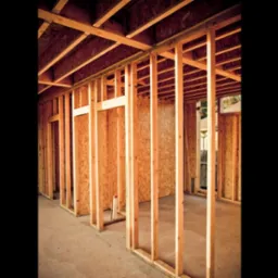 Wnętrze w trakcie budowy z widoczną drewnianą konstrukcją ścian i stropu, płyty OSB w tle, surowy beton na podłodze.