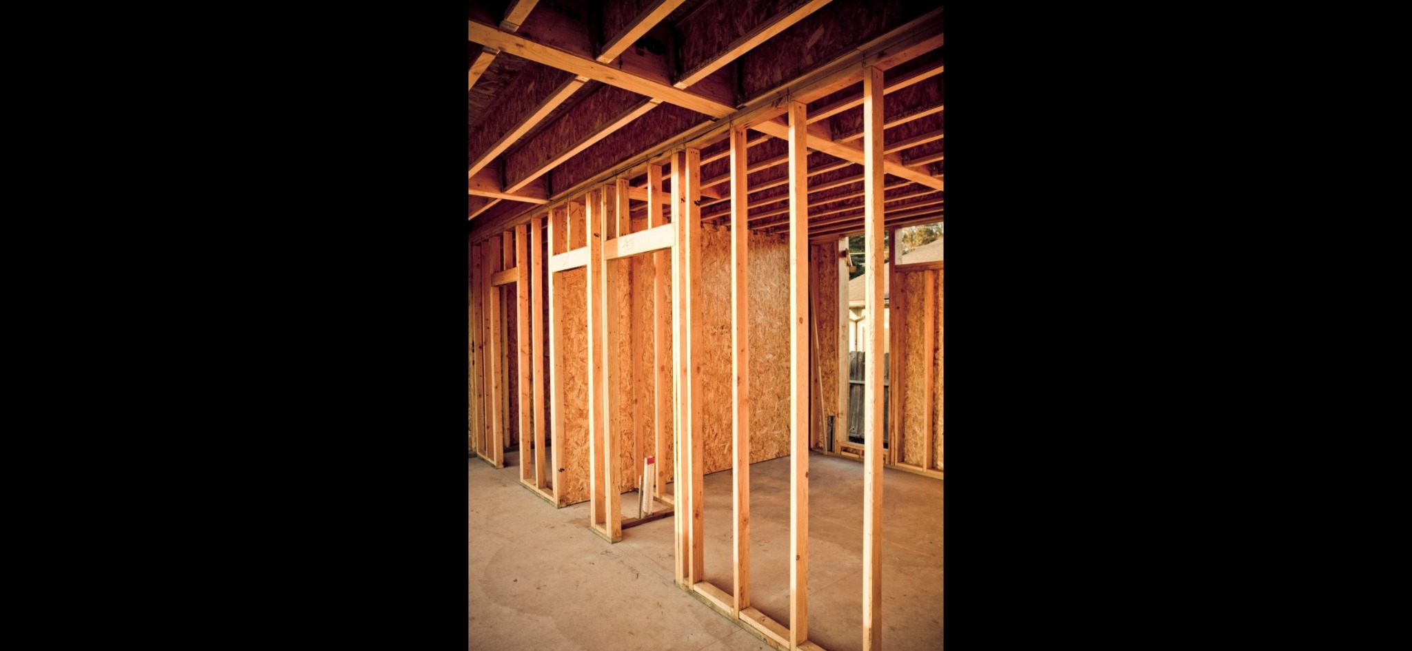 Wnętrze w trakcie budowy z widoczną drewnianą konstrukcją ścian i stropu, płyty OSB w tle, surowy beton na podłodze.