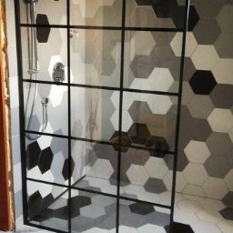 LAVATO Grzegorz Filipczyk - Kabina prysznicowa z czarnymi profilami, heksagonalne płytki w odcieniach szarości na ścianach i podłodze, marmurowe płytki pod kabiną, deszczownica zamontowana na suficie.