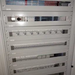 Rozdzielnica elektryczna z widocznymi bezpiecznikami, listwami zaciskowymi i wyłącznikiem, oznaczona numerami sekcji od 1 do 6, z opisami zakresów numerów bezpieczników w każdej sekcji.