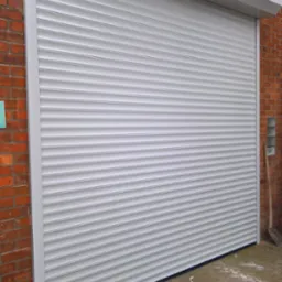 Zamknięta, szara roleta zewnętrzna zamontowana na ceglanym budynku, widoczna z bliska.