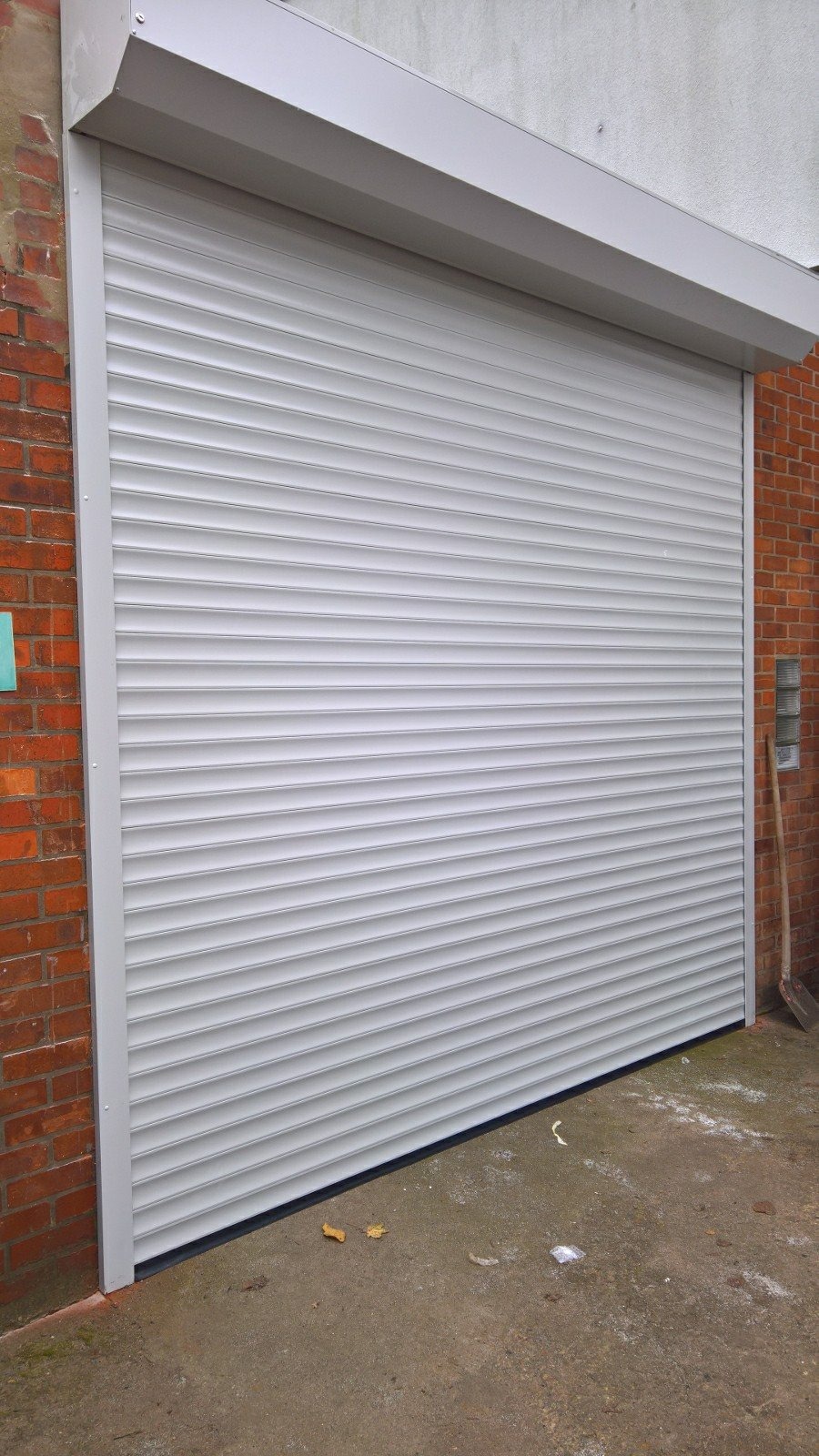 Zamknięta, szara roleta zewnętrzna zamontowana na ceglanym budynku, widoczna z bliska.