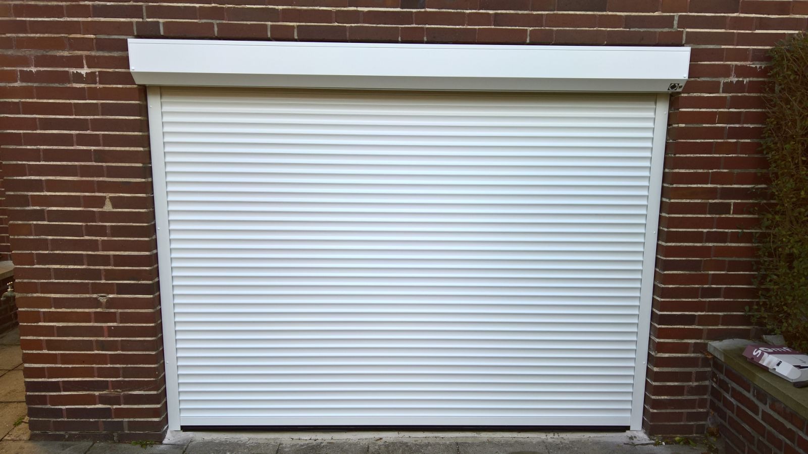 Zamknięta biała roleta zewnętrzna zamontowana na ceglanym garażu, widok z przodu.