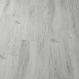 Artur Fraszczak - Jasnoszare panele podłogowe z widocznym grzejnikiem żeliwnym przy ścianie.