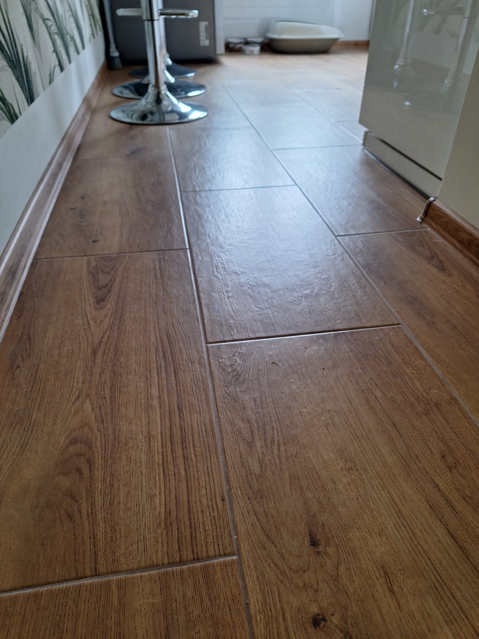 Ułożone brązowe panele podłogowe imitujące drewno, widoczne chromowane nogi hokerów i fragment białej szafki, realizacja w Dzierżoniowie.