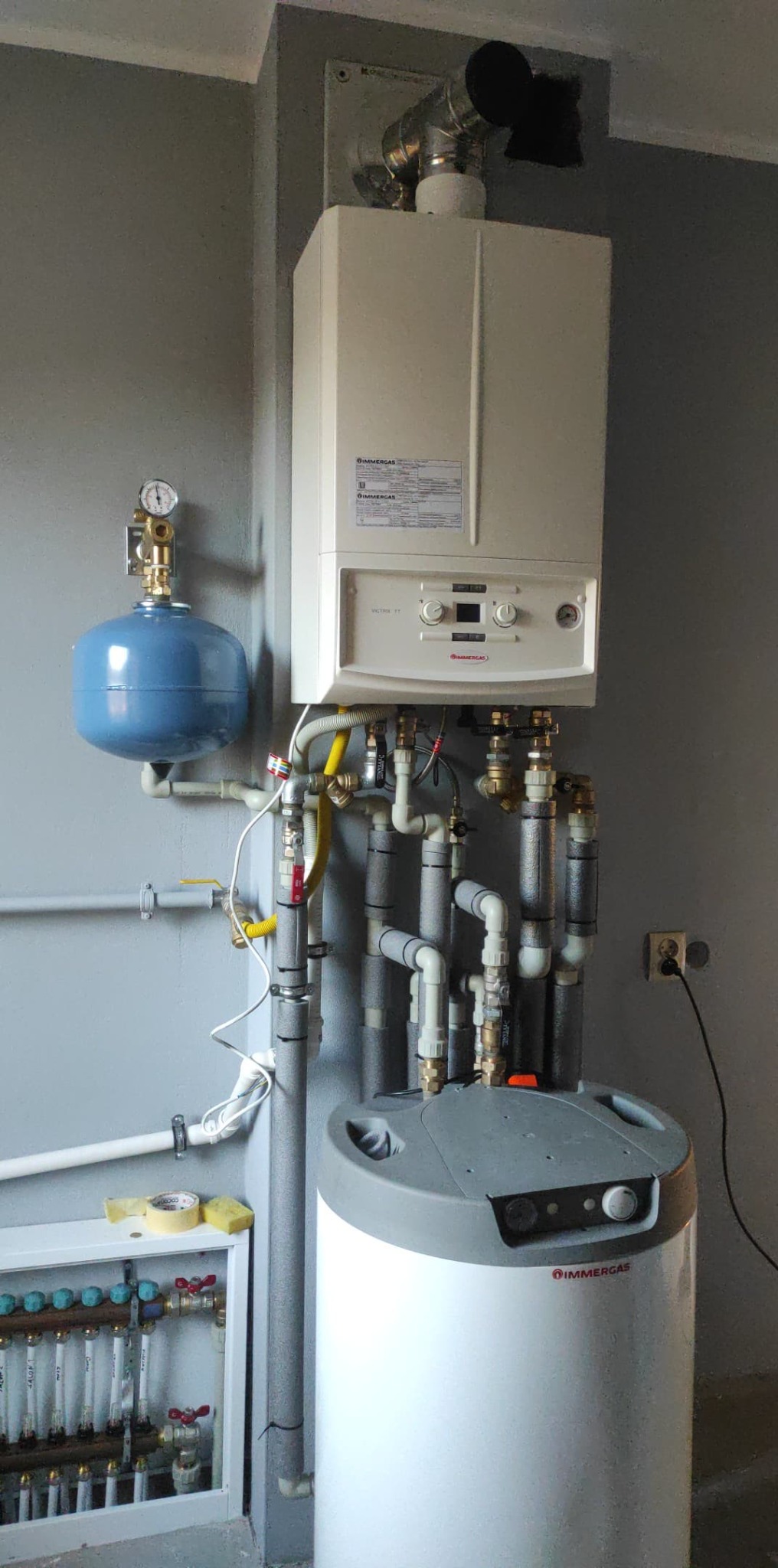 Zainstalowany piec gazowy Immergas w Pabianicach z podłączonym zasobnikiem ciepłej wody i osprzętem hydraulicznym, widoczny także rozdzielacz ogrzewania podłogowego.