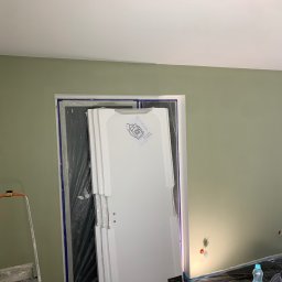 Oleksandr Kirichenko - Ściana pomalowana na oliwkowy kolor, zabezpieczone drzwi folią, drabina malarska. Widoczne gniazdka elektryczne. Etap prac wykończeniowych w mieszkaniu.