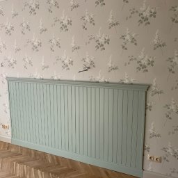 Oleksandr Kirichenko - Ściana z tapetą w kwiaty i panelami ściennymi w odcieniu zieleni, parkiet w jodełkę. Widoczne gniazdka elektryczne. Dekoracyjne wykończenie wnętrza.