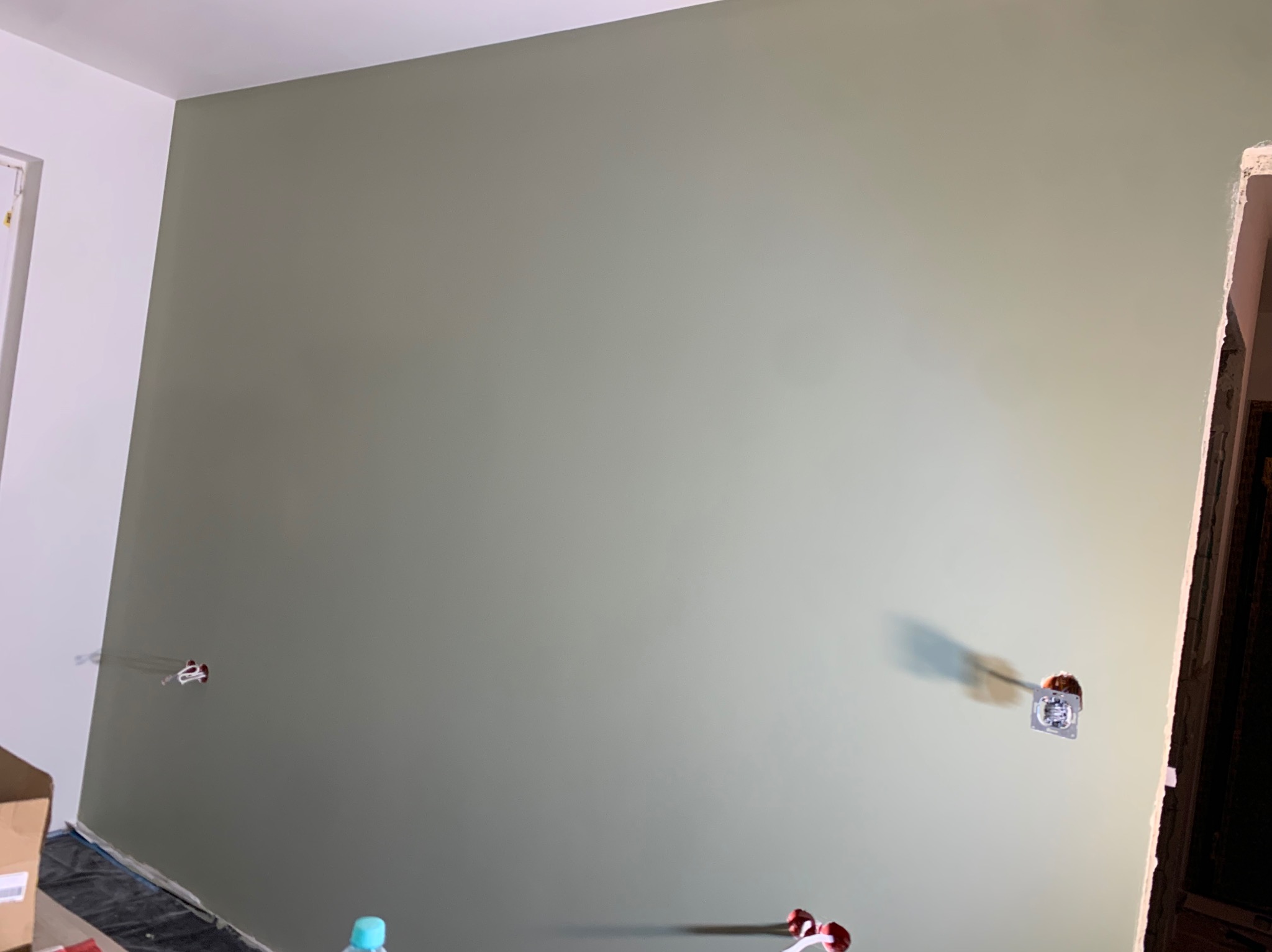 Świeżo pomalowana ściana w odcieniach zieleni z widocznymi gniazdkami elektrycznymi. Fragment białej ściany po lewej stronie. Prace wykończeniowe w trakcie.