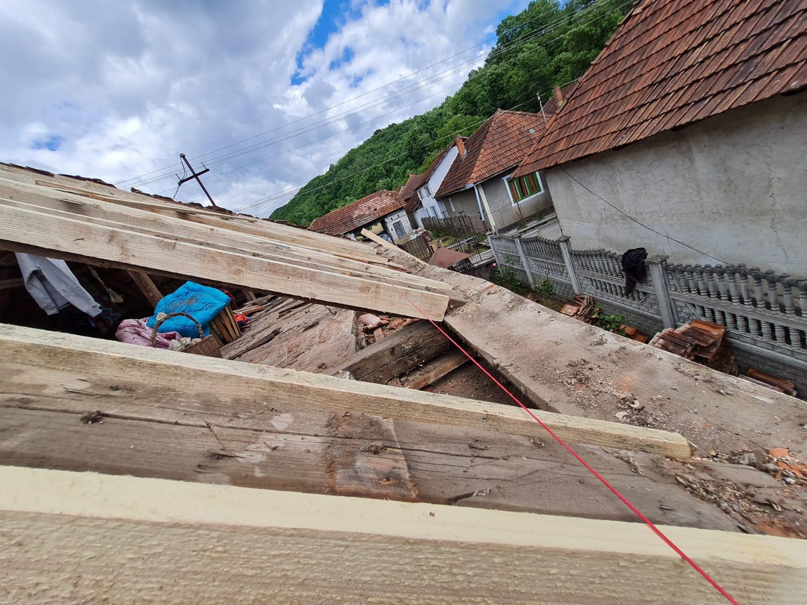 Dach w trakcie naprawy: widoczne drewniane elementy konstrukcyjne, częściowo usunięte stare pokrycie, w tle domy i zalesione wzgórze. Czerwona linka wyznacza linię.