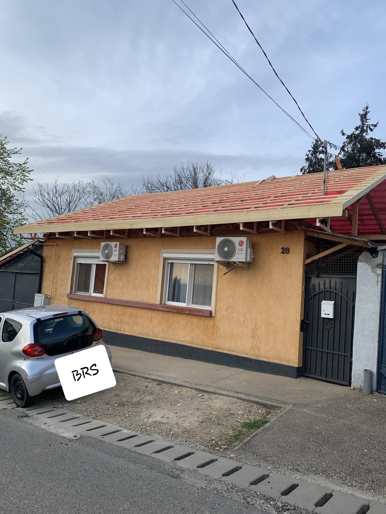 Dom jednorodzinny w trakcie wymiany dachu, widoczne krokwie i łaty. Częściowo zdjęte stare pokrycie. Na elewacji zamontowane klimatyzatory.