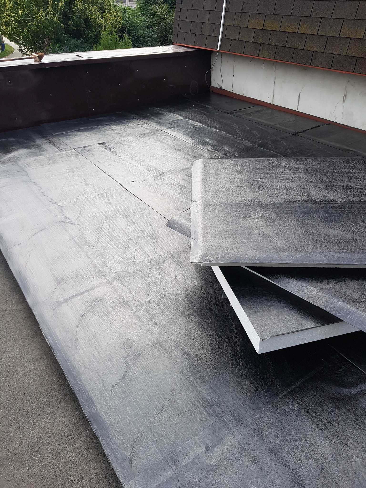 Widok z góry na płaski dach pokryty papą termozgrzewalną, z fragmentami izolacji termicznej przygotowanymi do montażu.