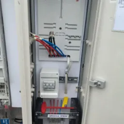 Otwarta skrzynka elektryczna z widocznymi przewodami (czerwone, niebieskie, czarne), bezpiecznikami Eaton, listwą zaciskową z oznaczeniem 'Granica Stron' oraz elementami montażowymi.