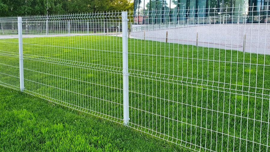 Nowoczesne, białe ogrodzenie panelowe z metalu, zamontowane na trawniku w Poznaniu, z budynkiem biurowym w tle.