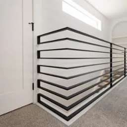 Nowoczesna balustrada schodowa z czarnych, poziomych profili, tworząca geometryczny wzór. Białe ściany i jasna podłoga podkreślają minimalistyczny design.