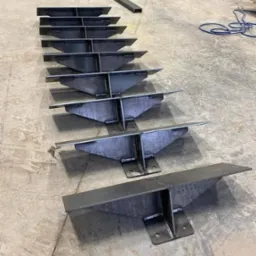 Rząd spawanych, metalowych wsporników schodowych ułożonych na betonowej podłodze, ukazujących precyzję wykonania i solidność konstrukcji.