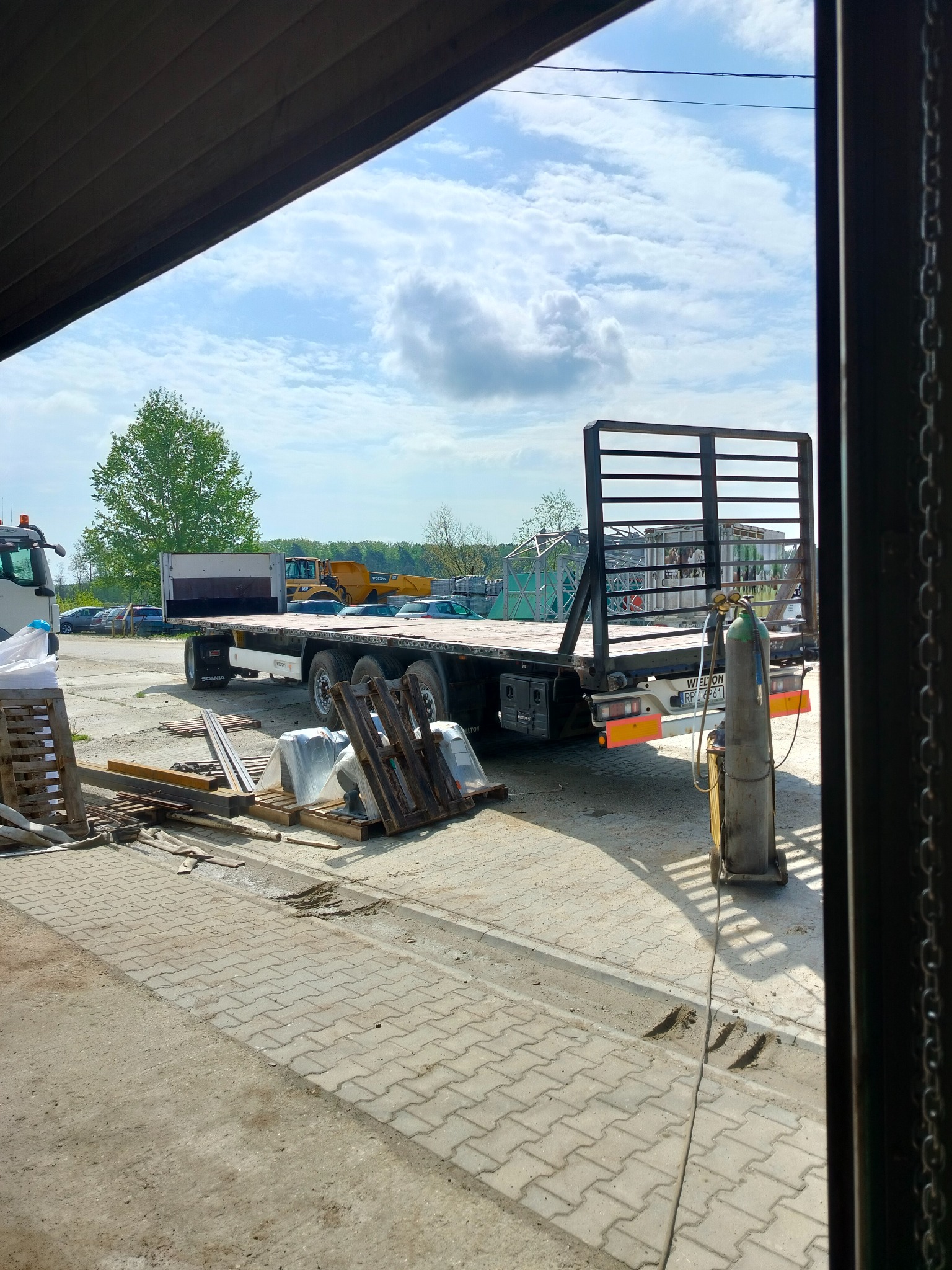 Ciężarówka z metalową konstrukcją na platformie, widoczna butla spawalnicza i elementy metalowe, sugerujące prace ślusarskie lub spawalnicze.