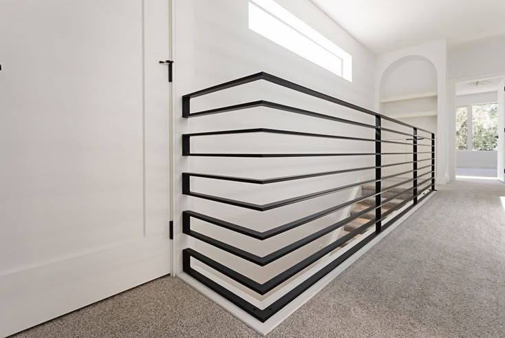 Nowoczesna balustrada schodowa z czarnych, poziomych profili, tworząca geometryczny wzór. Białe ściany i jasna podłoga podkreślają minimalistyczny design.