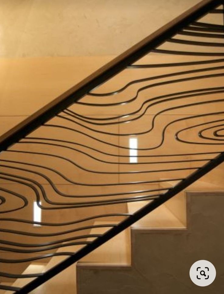 Stylowa, czarna balustrada schodowa z unikalnym wzorem falistych linii, na tle jasnych schodów. Ujęcie z dołu, podkreślające design.