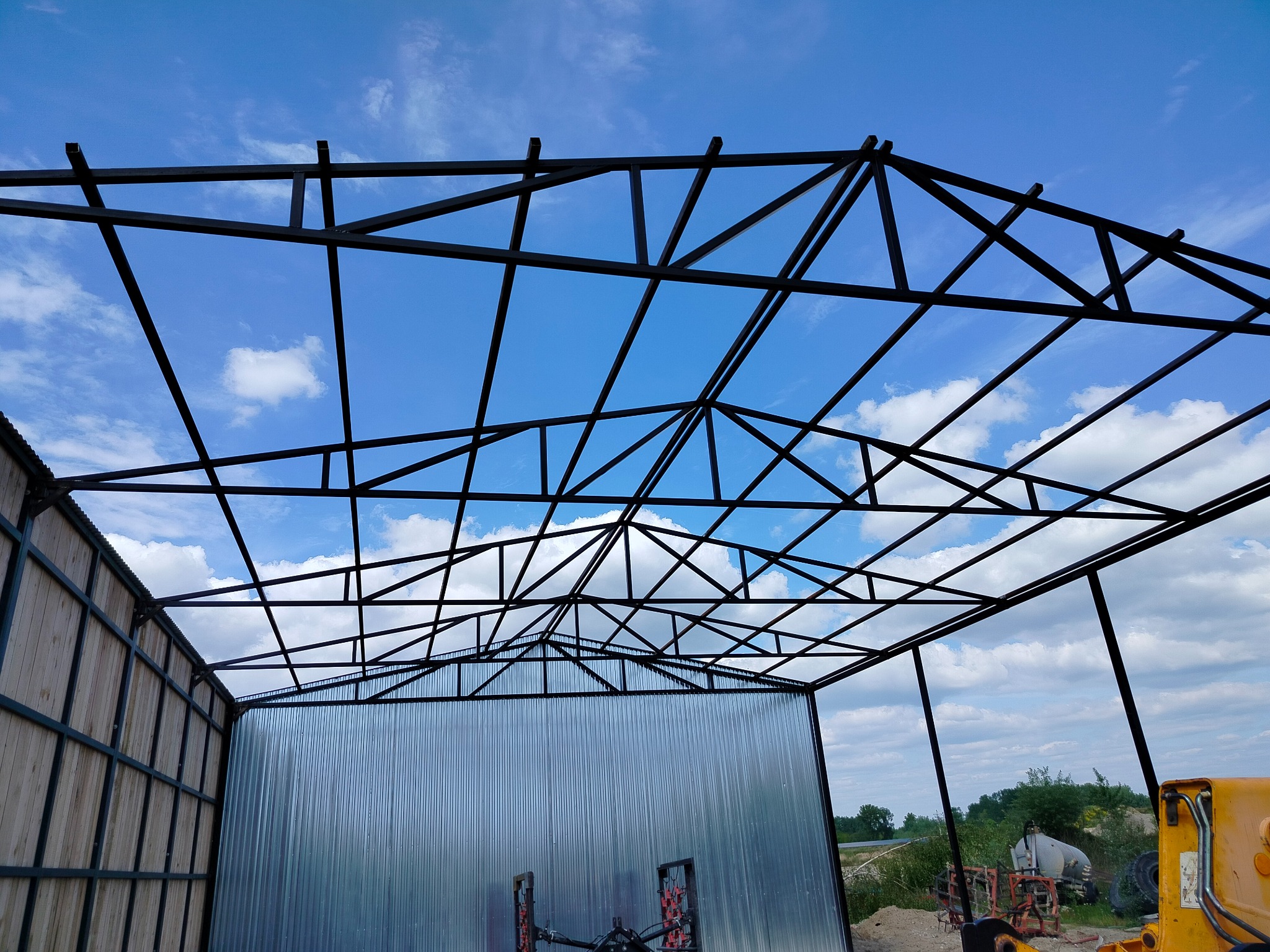 Konstrukcja stalowa hali w trakcie budowy, widok od dołu na metalowy szkielet i fragment obudowy, błękitne niebo w tle.