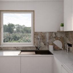 Minimalistyczna kuchnia z oknem na ogród. Białe szafki, marmurowy backsplash, czarny zlew i bateria. Na blacie deska do krojenia i przyprawy. Jasne, naturalne światło.