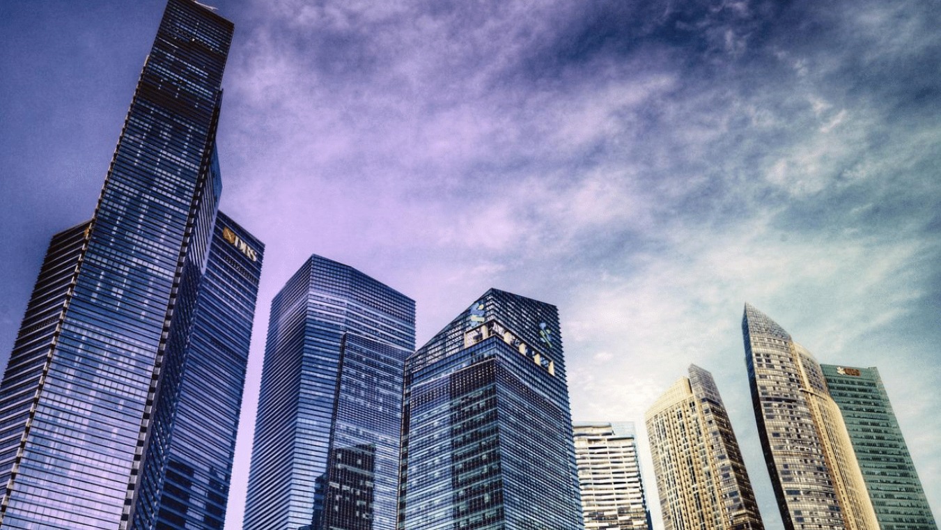 Wysokie, nowoczesne biurowce ze szklanymi fasadami, widoczne z dołu pod kątem, na tle błękitnego nieba z chmurami.