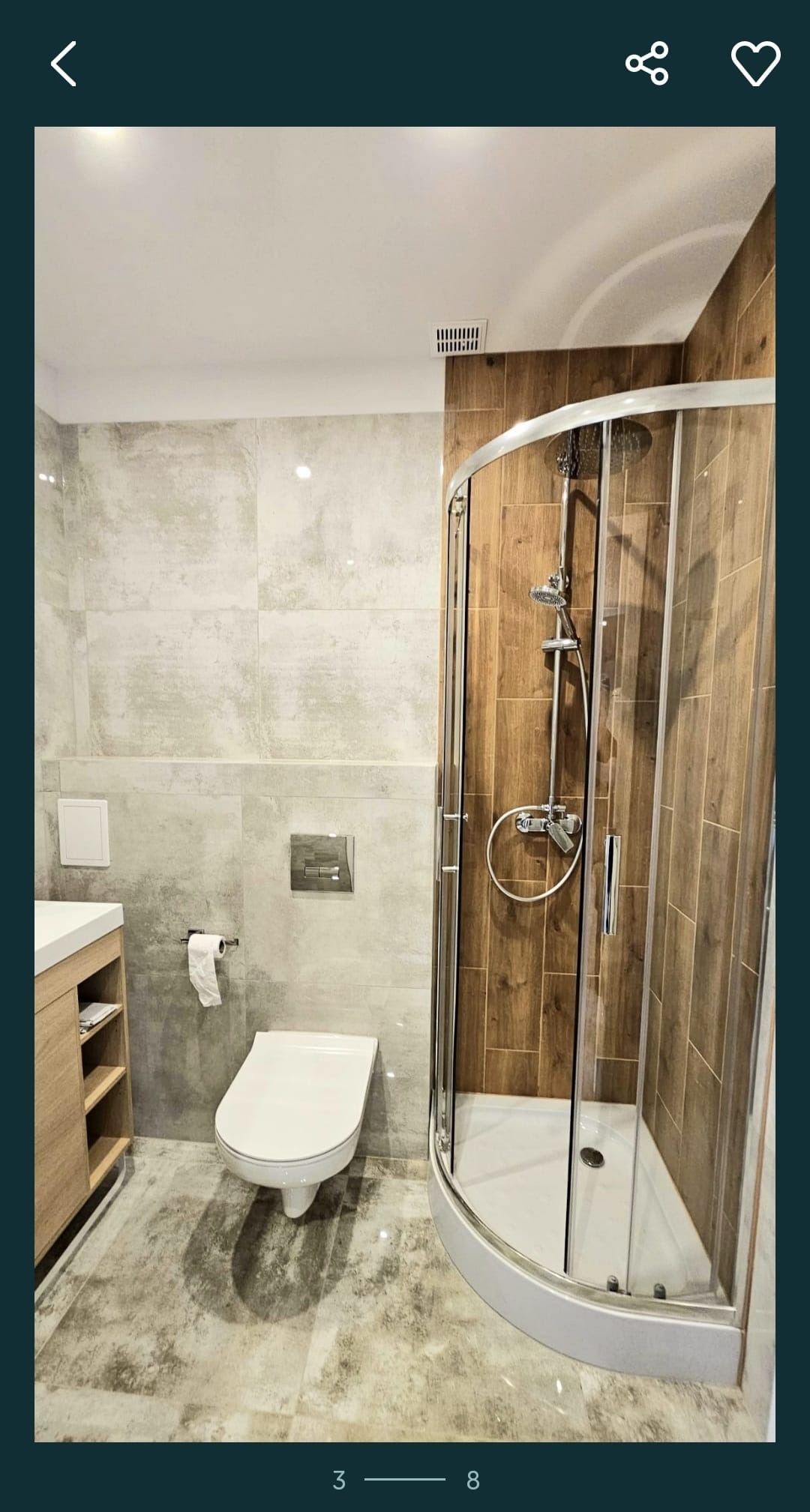 Nowoczesna łazienka z kabiną prysznicową narożną, toaletą wiszącą i umywalką z szafką, wykończona płytkami w odcieniach szarości i brązu, z widoczną armaturą chromowaną.