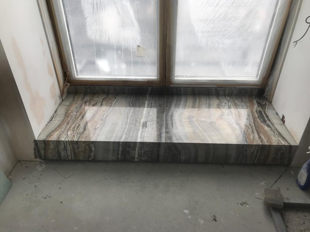Onyksowy parapet wewnętrzny zamontowany pod oknem dachowym, widoczne ślady prac wykończeniowych na ścianie i podłodze.