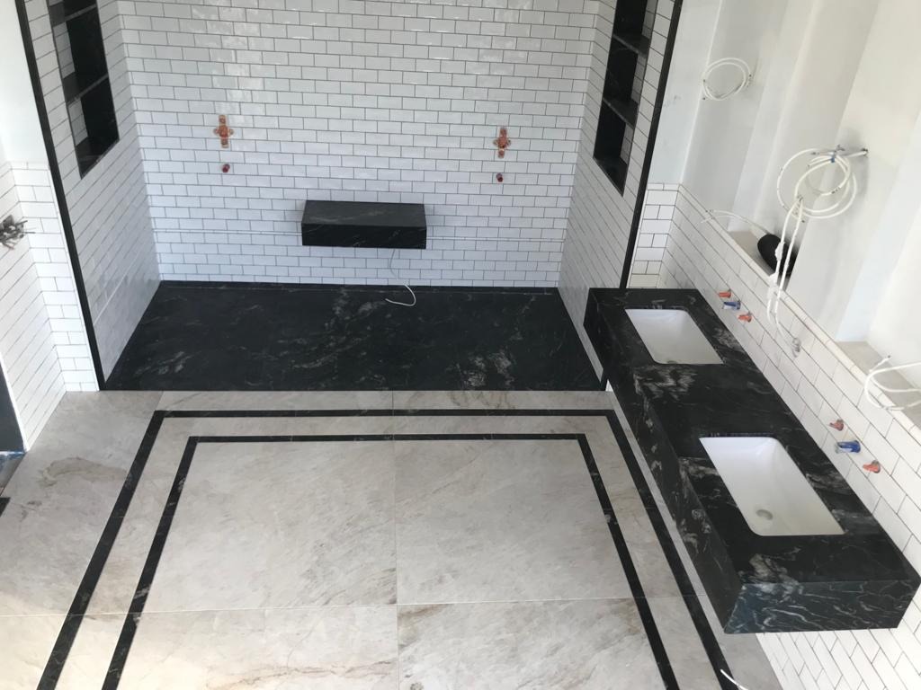 Łazienka w trakcie wykończenia: białe płytki ścienne typu metro z czarną fugą, czarna marmurowa podłoga prysznicowa i blat umywalkowy, jasne płytki podłogowe z czarną obwódką, widoczne instalacje...