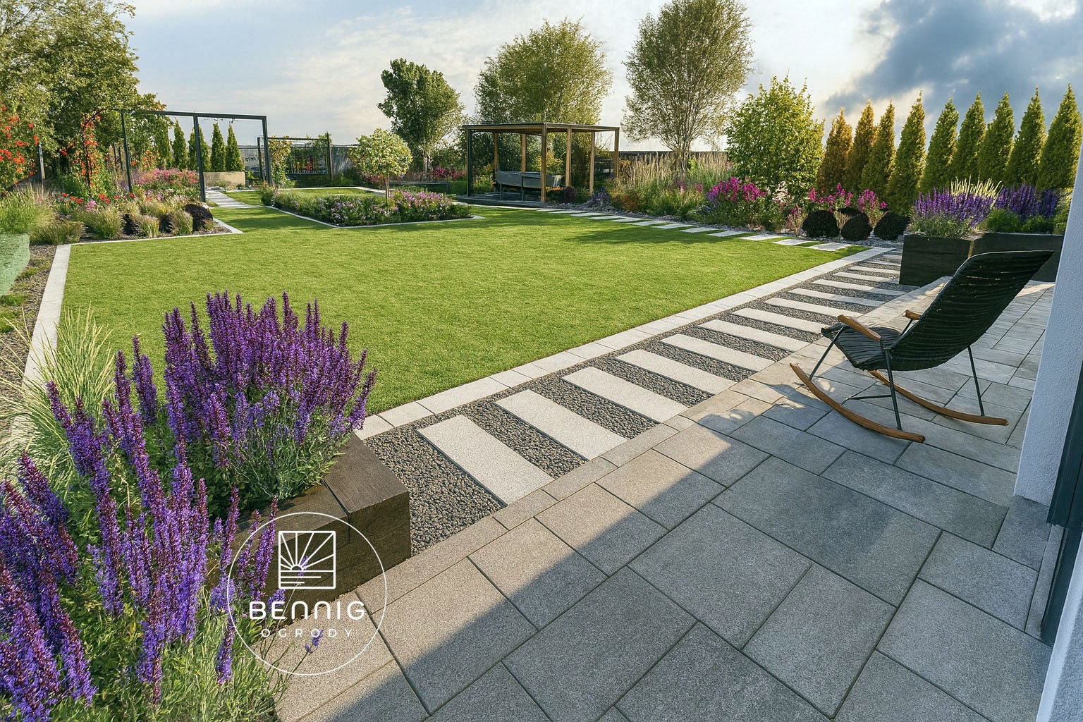 Nowoczesny ogród z równo przystrzyżonym trawnikiem, ścieżką z płyt i żwiru oraz fioletowymi kwiatami. W tle altana i drzewa. Na pierwszym planie fotel bujany.