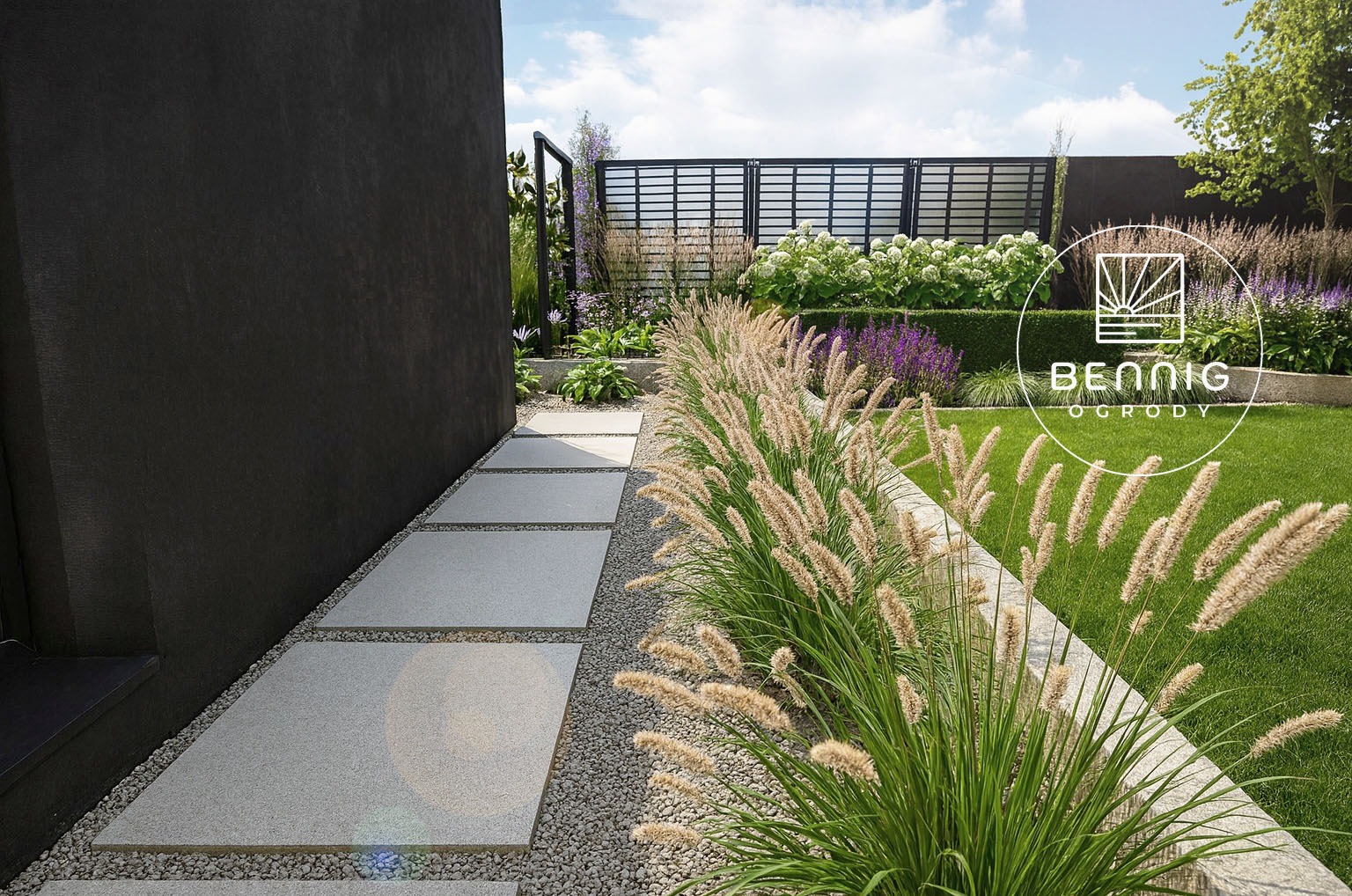 Nowoczesny ogród z minimalistycznym chodnikiem z płyt, ozdobnymi trawami i geometrycznym ogrodzeniem. Widoczny fragment budynku o ciemnej elewacji.