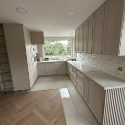 Perfect-Dom Piotr Dombrowski - Jasna kuchnia z mozaiką na ścianie i parkietem w jodełkę. Nowoczesne szafki z subtelnymi uchwytami i blatem z szarego kamienia. Duże okno wpuszcza naturalne światło.