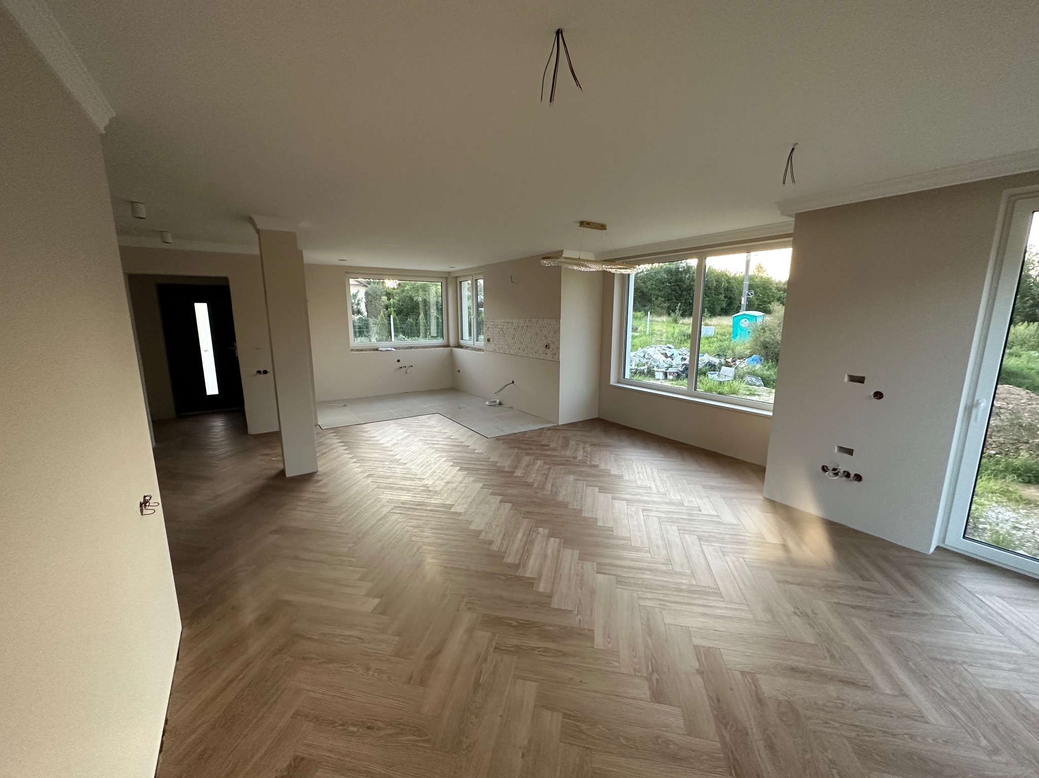 Jasne, przestronne wnętrze po remoncie z parkietem ułożonym w jodełkę. Widoczne gładkie ściany, okna z widokiem na zieleń i przygotowane punkty elektryczne.