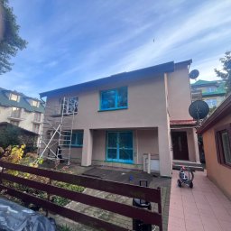 Michał Obarzanek Clean Brothers - Dom jednorodzinny w trakcie przygotowań do malowania elewacji. Okna zabezpieczone folią, rusztowanie przy ścianie. Widoczne narzędzia malarskie.