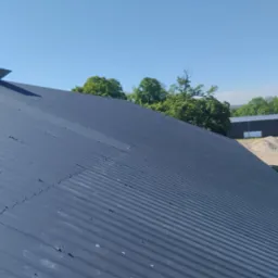 Nowy, ciemnoszary dach z blachy trapezowej, widok z góry, w tle drzewa i budynek magazynowy.