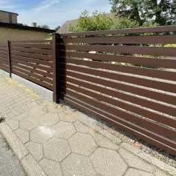 AMTRANS ANTONI OGIERMAN - Nowoczesne, poziome ogrodzenie panelowe w kolorze brązowym, z widoczną kostką brukową i budynkiem w tle.