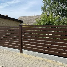 AMTRANS ANTONI OGIERMAN - Brązowe ogrodzenie poziome z paneli na betonowej podmurówce, widok z zewnątrz na tle domów i zieleni.