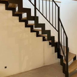 AMTRANS ANTONI OGIERMAN - Nowoczesne schody metalowe z drewnianymi stopniami i minimalistyczną balustradą w surowym wnętrzu, widoczne gniazdko elektryczne w ścianie.