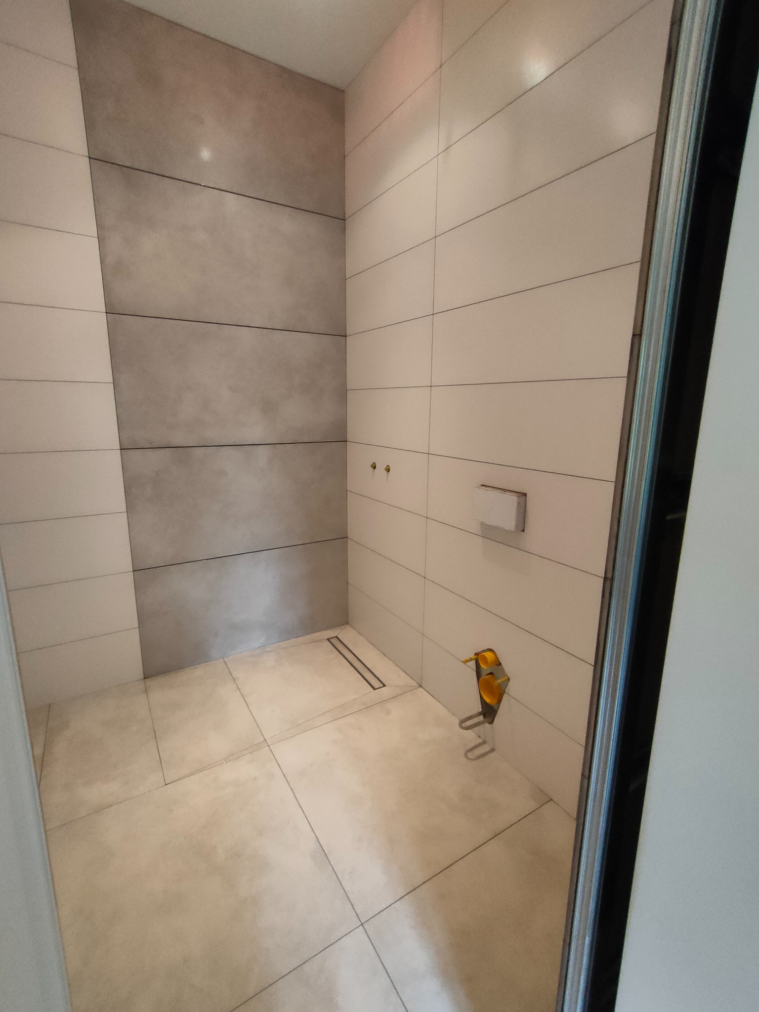 Nowoczesna kabina prysznicowa w Krotoszynie z beżowymi płytkami w różnych odcieniach szarości i beżu, z odpływem liniowym i widocznymi elementami instalacji.